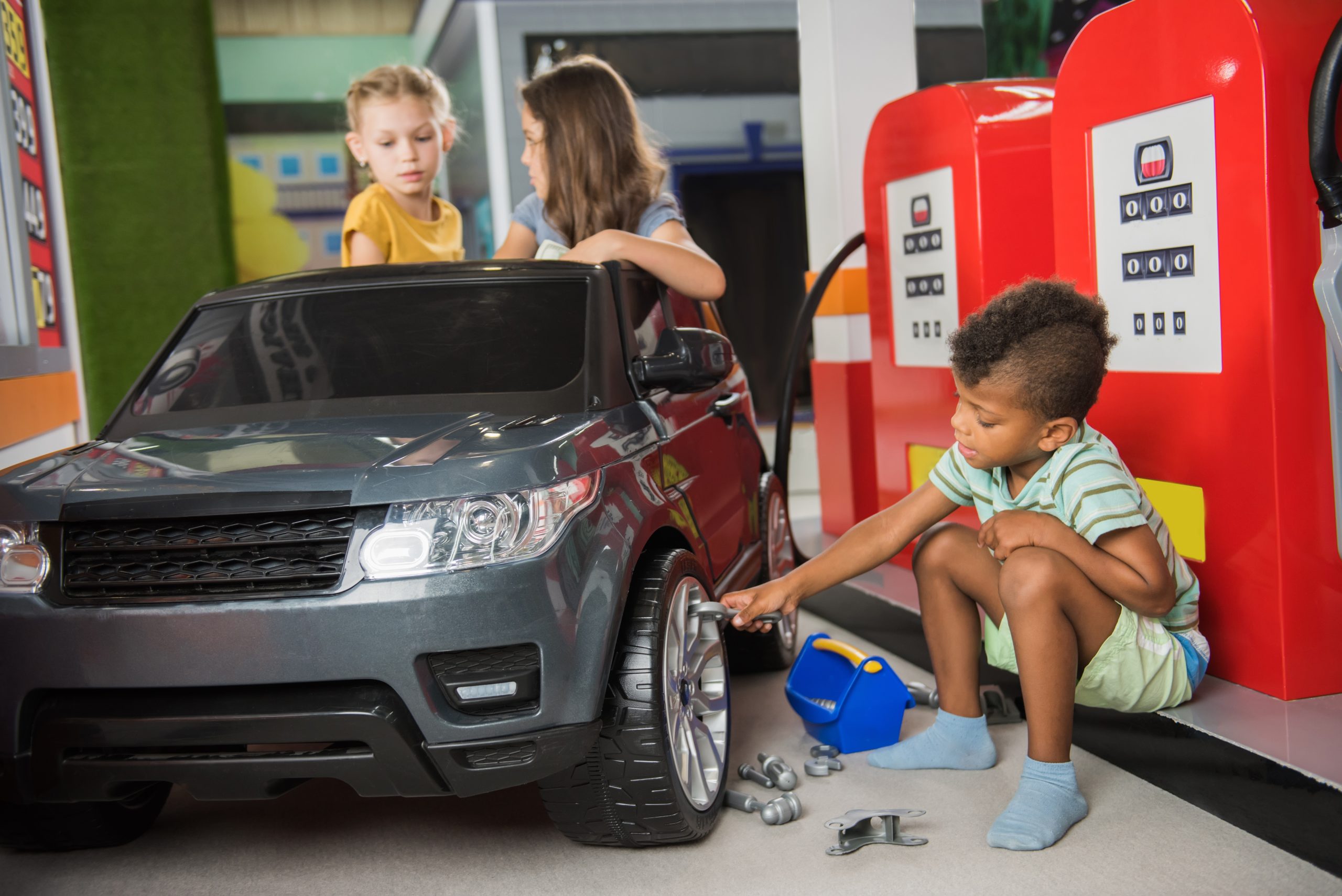 Cute little girls at car service station in playroom. Children playing gas station at entertainment center. Kids role games.